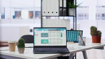 Financial analyst workspace featuring laptop and tablet displaying stock market data and statistics. Devices on desk in office next to paperwork with forex trading economic analytics figures video