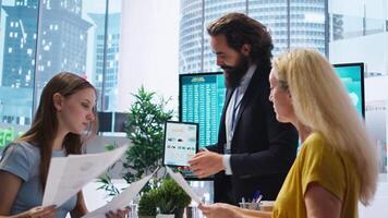 Financial adviser presents market analytics to clients using large display and tablet device, teaching how to build portfolio. Broker showing stock exchange charts to parent and girl, camera A video