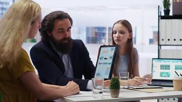 Financial advisor showing statistical graphs on tablet to clients, analyzing market trends to optimize their income. Mother and daughter checking investment plan on device, camera B video