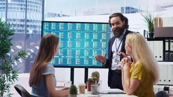 Broker investor in office offering financial advice to clients, looking at stock exchange volatility on big screen. Financial advisor analyzing market shares growth with mother and daughter, camera B video