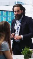 Vertical Financial adviser presents market analytics to clients using large screen, emphasizing data driven decision making. Broker showing statistical charts about stock exchange indicators, camera A video