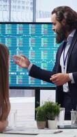 Vertical Broker in office providing stock exchange valuation analysis for clients looking to make more money. Financial advisor looking at market shares on big screen, helping people make investments, camera B video