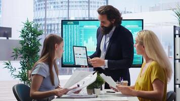 Financial adviser presents market analytics to clients using large display and tablet device, teaching how to build portfolio. Broker showing stock exchange charts to parent and girl, camera B video