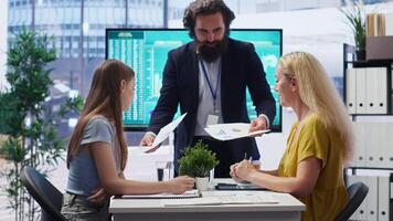 Financial advisor showing data graphs on big screen to customers, analyzing market trends to do forecasting. Mom and gen Z girl checking investment plan on display made by agent, camera B video