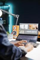 Black woman working at her desk, using a laptop and typing on the keyboard. She is immersed in her work, browsing and editing content, showcasing her creativity and productivity. photo