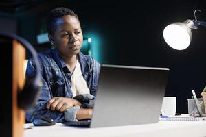 Tired African American college student at desk with a laptop, stressed and overwhelmed by projects and studies. Young black woman feeling unwell is looking at and reading emails on wireless computer. photo