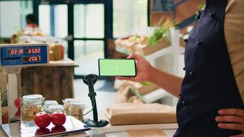 Merchant with phone greenscreen at store counter, presenting isolated chromakey display on mobile gadget. Farmer and vendor using modern copyspace template with mockup technology. photo