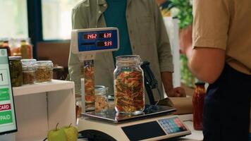 Salesperson in convenience store weighs fresh produce and groceries for middle eastern shopper by using digital scale at register. Retailer in local shop selling bulk pantry goods. Handheld shot. photo