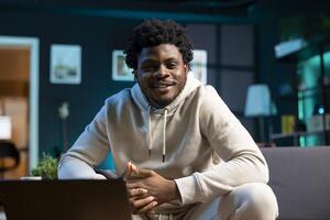 Portrait of upbeat self employed man working from home using laptop to send emails. Joyous BIPOC man typing on notebook keyboard, composing documents in order to deliver finalized project files photo