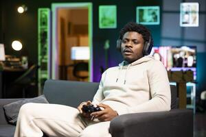 BIPOC gamer at home sitting down on couch, enjoying games on laptop during leisure time. Man sitting on couch in apartment, playing videogame on notebook, relaxing after work photo
