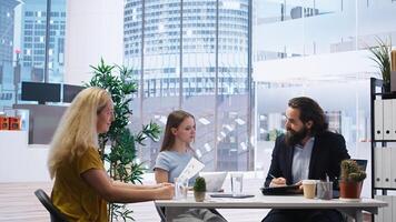 Financial advisor discussing with customers, recommending optimal insurance policies. Agent informing parent and daughter of best investment strategies, offering statistics, camera A photo