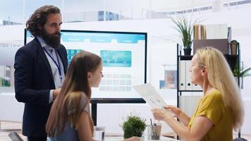 Financial advisor discussing with clients, recommending suitable financial products such as mutual funds. Agent teaching parent and daughter how to invest, offering statistical graphs, camera B photo