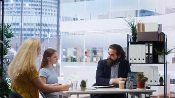 Financial advisor discussing with customers, recommending optimal insurance policies. Agent informing parent and daughter of best investment strategies, offering statistics, camera B photo