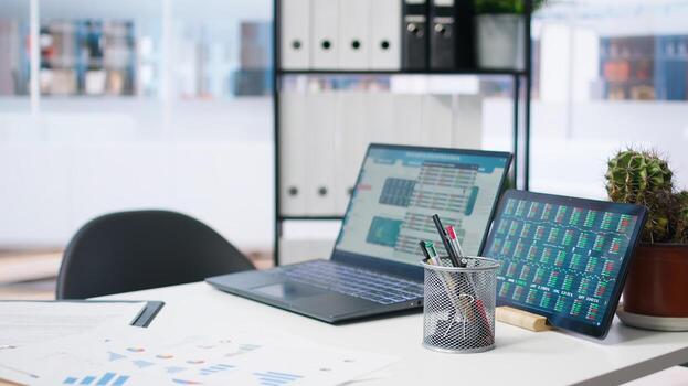 Laptop device on office desk in empty workspace showing volatile stock exchange prices going up and down. Brokerage firm with forex trading platforms indexes on notebook screen photo