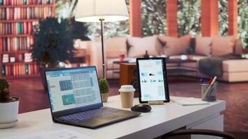 Empty home office with tablet and laptop showing infographics and accounting data, financial business reports. Space used for a specialist to study the market and work on economy analysis. photo