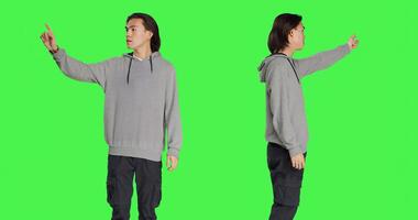 Person indicating left or right directions on camera, pointing to both sides and recommending another path. Asian young man advising someone to go that way, greenscreen backdrop. photo