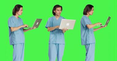 Specialist reading patient information on laptop, using wireless computer before starting healthcare checkup. Young man working as medical assistant, using portable pc on greenscreen. photo