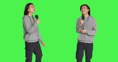 Cool person doing karaoke session on camera, using microphone to sing modern songs and lyrics. Young adult having fun over greenscreen backdrop, creating music and singing tunes. photo