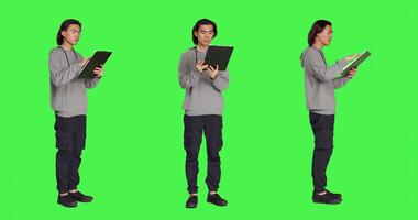 Asian adult reading information on files, thinking about annotations on clipboard papers or taking notes for finalization. Young guy writing on documents, standing against greenscreen. photo