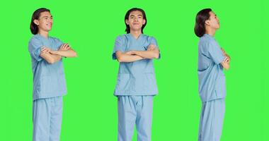 Friendly nurse posing in studio with confidence, wearing clinical uniform and standing with arms crossed over greenscreen backdrop. Young medical assistant working in healthcare industry. photo