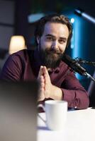Portrait of smiling content creator hosting online show in rgb lights studio, shooting vlog using professional microphone. Cheerful vlogger presenting informations during streaming service broadcast photo