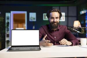 Smiling influencer talking to audience about recent news headlines, reading from mockup laptop. Cheerful man discussing with subscribers, presenting information from isolated screen notebook photo