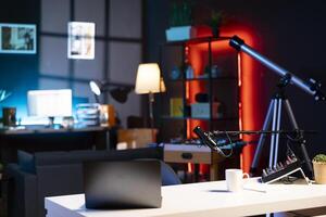 Internet production gear in empty home studio interior illuminated with RGB lights at night. Professional microphone, sound mixer and other content creation equipment in apartment room photo