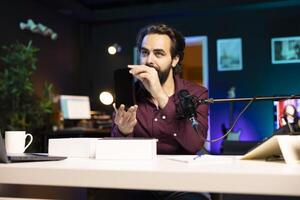 Tech guru reviewing latest mobile phone, filming internet show in neon lights studio, shooting technology vlog using professional microphone. Content creator presenting best smartphones on the market photo