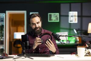 Content creator endorsing headphones for internet streaming platforms viewers, recording with cellphone on tripod stabilizer. Tech expert promoting music listening device in neon lit studio photo