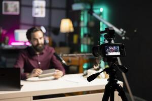 Focus on tech guru in blurry background doing technology review of wireless portable speaker. Close up shot of professional camera used by influencer to record music playing device review photo