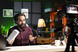 Tech influencer using professional camera and mic to film technology review of smartphone, doing unboxing . Man showing phone box to viewers, recording with high tech devices photo