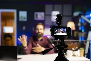 Focus on professional recording equipment used by media star in blurry background to film vlog channel intro. Close up of camera used by man to record himself greeting fans photo