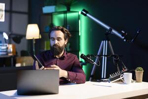 Tech engineer presenting tablet in entry level low budget price range, filming from dimly lit home studio. Viral tech content creator reviewing digital device in front of online audience photo