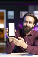 Tech guru assessing isolated screen smartphone performance, feeling happy with high quality components used. Portrait of smiling content creator shooting mobile phone review for online channel photo
