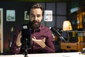 Tech guru presenting V mount battery, filming technology review using cellphone on tripod and professional microphone. Caucasian vlogger showcasing charging device specs, recording with phone photo