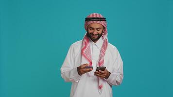 Joyful model using card to make payment while shopping on clothing store website using smartphone app. Middle eastern adult in islamic costume doing banking transfer to buy on sale. photo