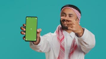 Muslim man on mobile device with greenscreen theme, Putting forward isolated mockup chromakey on smartphone display. Young arabic person exhibits blank copyspace template design. photo