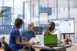 Elderly clients discussing with advisor about securing a pension plan, having a chroma key on laptop in modern office. Senior people establishing a retirement option for life insurance. photo