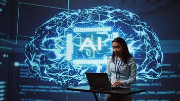 Technician in high tech workspace managing call center tasks, speaking into headset while doing monitoring with laptop. AI company employee talking with clients through headphones mic, camera B photo