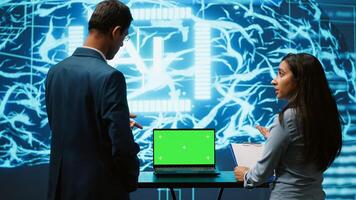 Startup coworkers looking over charts, using AI software on mockup laptop to take data driven decisions. Teamworking colleagues developing artificial intelligence solutions for company, camera A photo