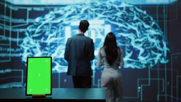 Engineers use green screen tablet and AI neural networks modeled after human brain to solve complex problems. Workers using artificial intelligence and mockup device to look at company data, camera B photo