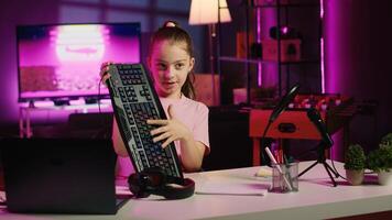Cute girl in studio using camera to review gaming keyboard, mouse and headphones. Joyous youngster show host filming electronics haul, presenting wired computer peripherals to viewers photo