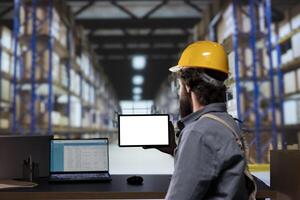 Stock manager looking at blank tablet display in storage room, reviewing list of cargo invoices for distribution. Engineer handling supply chain management and shipments, uses white screen. photo