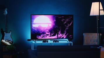 Zoom in shot on TV screen showing 3D render animations in empty stylish neon lit home studio interior. Modern apartment illuminated with RGB lights at night and artwork decorating the walls photo