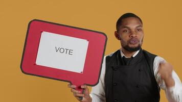 Waiter does an advertisement for politics and showing a speech bubble with the message to vote, standing against yellow background. Restaurant staff holds a cardboard sign. Camera A. video