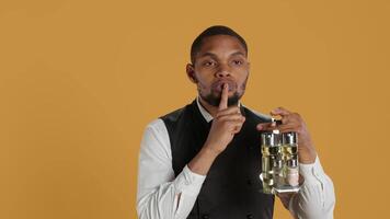 Catering staff waiter doing a mute sign for silence and privacy, keeping quiet while he carries cruet set with condiments for customer satisfaction. Shows a hush symbol to keep secret. Camera A. video