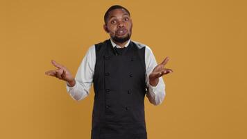 Professional waiter showing clueless sign and being unsure, shrugging and saying i dont know in studio. Confused butler staff in apron feeling uncertain and doubtful about something. Camera B. video