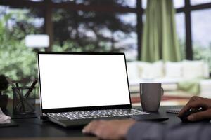 Billionaire director unwinds in front of white display on laptop, luxurious mountain cabin. In a successful business corporation, general manager operates with blank mockup screen on pc. photo