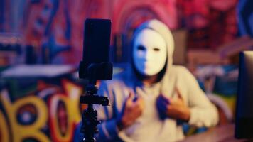 Masked hacker threatening to not stop flooding servers and launch DDoS attack on website making it crash unless his demands are not met, filming blackmail in underground bunker photo