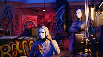 Hacker group members doing online terrorism acts, filming ransom with smartphone in hidden underground base, threatening to release stolen sensitive data publicly if payout demands are not met photo